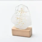 Transparent crystal with engraved scientific symbols on a wooden base.