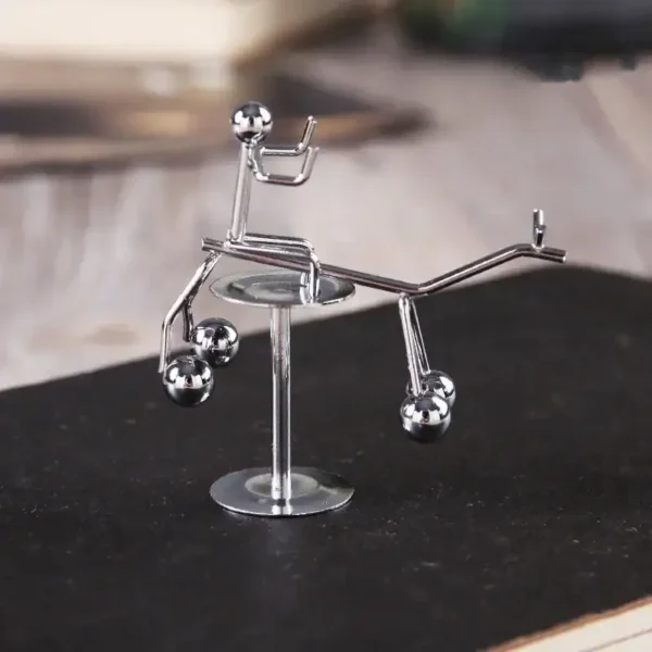 Miniature metallic sculpture of a balancing seesaw with small spheres and a figure, demonstrating physics principles.