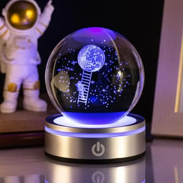 Illuminated glass globe featuring a moon scene with an astronaut climbing a ladder towards the moon, set on a sleek base with LED lighting. Perfect for science enthusiasts and educational decor.