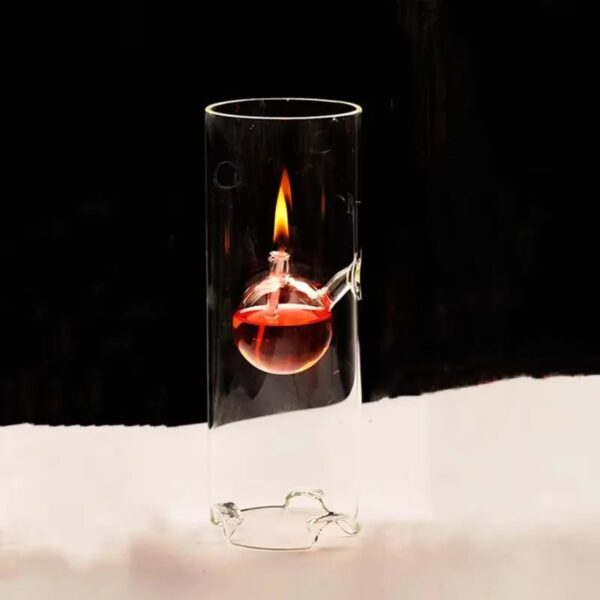 A glass test tube with a small round-bottom flask inside, containing a red liquid and a visible flame, demonstrating a science experiment.