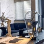 A creative lighting fixture designed as a giant light bulb with a vintage filament, placed on a modern living room table alongside decorative items and an open book.