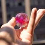 Hand holding a colorful magnetic glass marble with pink, gold, and purple swirls, showcasing a shiny, smooth surface.