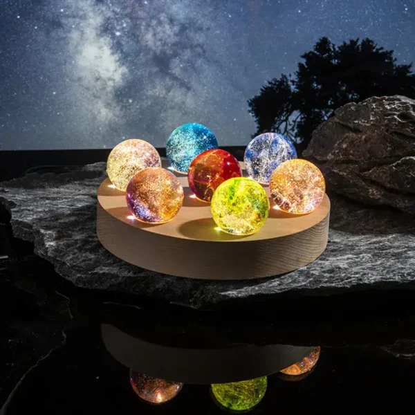 Colorful galaxy marbles illuminated by LED lights, displayed on a wooden platform outdoors at night with starry sky background.