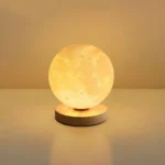 Moon-shaped LED lamp emitting a warm glow, resting on a wooden stand.