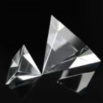 Close-up of a reflective glass pyramid sculpture on a black background, showcasing its sharp edges and geometric design.