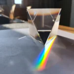 Clear diamond-shaped prism dispersing light into a vibrant rainbow spectrum on a dark surface.