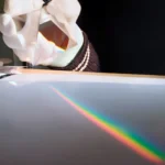 Rainbow light spectrum projection on a surface with a gloved hand holding a prism.