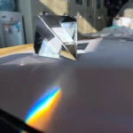 Small glass prism cube demonstrating light refraction and dispersion with rainbow spectrum on a smooth surface. Perfect for science experiments and educational displays.