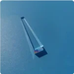 A clear acrylic prism with a rainbow reflection on a blue surface.