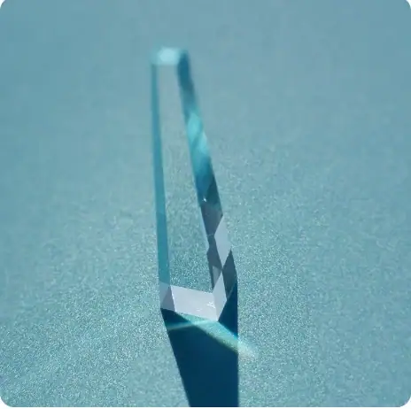 Close-up of a clear, triangular glass prism casting a colorful light reflection on a smooth surface.