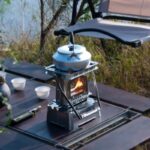 Camping stove with kettle on outdoor table in nature setting.