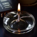 Close-up of a lit candle in a glass holder, showcasing the gentle flame and reflective surface, ideal for science decor and educational displays.