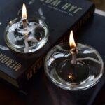 Glass tealight candles with flames on a dark surface, placed on a black book titled "MEMO" with scientific and educational themes.