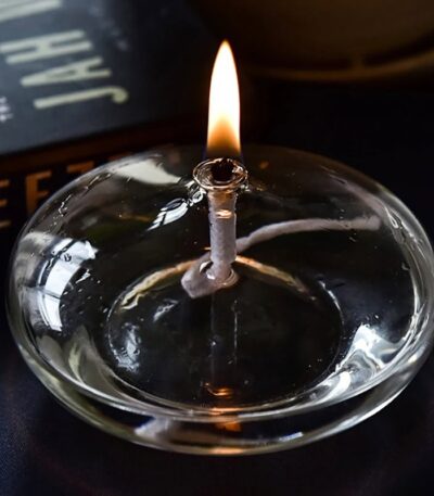 Close-up of a lit candle in a glass holder, showcasing the gentle flame and reflective surface, ideal for science decor and educational displays.