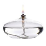 Miniature oil lamp with a lit flame, made of clear glass and metal, used for decorative or educational purposes.