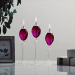 Pink glass candle holders with lit flames, elegant and decorative, placed on a white surface with a minimalist background.