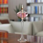 Glass candle holder with a lit candle and pink liquid inside, placed on a wooden surface in a cozy indoor setting.