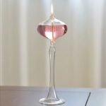 Elegant glass candle holder with pink liquid wax and a lit flame, creating a warm and inviting ambiance.
