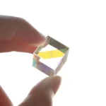 Close-up of a small optical prism held between fingers, demonstrating light dispersion and refraction effects.