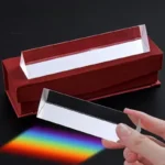 Hand holding a spectrum prism projecting a rainbow of light onto a black surface, with a red display box in the background. Ideal for science education and optical experiments.