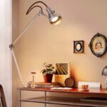 Modern adjustable desk lamp illuminating a workspace with decorative items, including a potted plant, framed artwork, and vintage clocks, creating a cozy and inspiring science-themed environment.