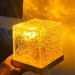 A glowing, textured ice cube-shaped lamp emitting warm yellow light, placed on a black base, creating a cozy and modern ambiance.