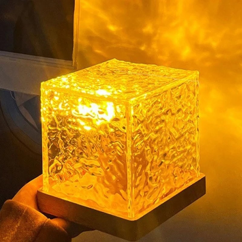 Light-up Ice Cube Lamp with Textured Surface A glowing, textured ice cube-shaped lamp emitting warm yellow light, placed on a black base, creating a cozy and modern ambiance.