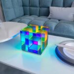 A vibrant, illuminated cube puzzle made of transparent, colorful geometric blocks arranged in a complex pattern on a white table.