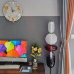 Bright computer monitor displaying a vibrant pattern of multicolored umbrellas, placed on a desk with a vase of flowers and a modern lamp in the background.