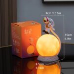 A glowing astronaut figurine holding a moon-shaped light, perfect for science-themed decor and educational purposes.