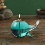 Whale-shaped glass oil lamp with a lit flame, designed for decorative and educational purposes.