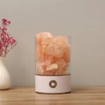 Salt rock lamp with Himalayan salt crystals in a clear glass container, placed on a wooden surface with a neutral background.