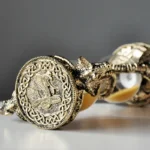 Close-up of a silver bracelet featuring an intricate ancient coin with a dragon motif, connected by detailed chain links, on a neutral background.