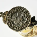 Close-up of a detailed medieval dragon coin pendant with intricate Celtic knot border, made of metallic material, showcasing craftsmanship and historical design.