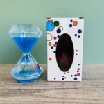 Colorful hourglass-shaped science toy with blue liquid and bubbles, next to a decorated box with circular patterns.