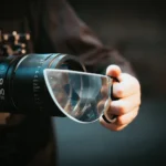 Hand holding a magnifying glass with a camera lens in the background, showcasing scientific exploration and observation tools.