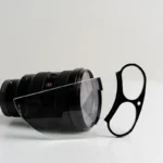 Close-up of a camera lens with a protective filter and a pair of glasses on a white background, showcasing photography equipment and accessories.