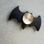 A black Batman logo-shaped fidget spinner with a metallic center, designed for stress relief and sensory play.