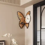 A decorative butterfly-shaped wall clock featuring a floral design on the butterfly wings and a white clock face with black numbers and hands, mounted on a beige wall.