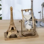 Miniature Eiffel Tower and hourglass on wooden surface, decorative science and travel-themed desk accessories for educational or aesthetic purposes.