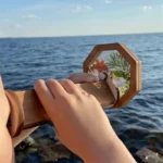 Handheld wooden mirror reflecting the sunset over the ocean.