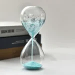 An image of a sleek glass hourglass filled with blue sand, demonstrating the passage of time through flowing grains. Perfect for educational displays or modern decor emphasizing science and time conce.