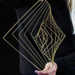 Intricate gold wire geometric sculpture held by a person against a dark background, showcasing modern abstract art design.
