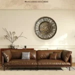 Stylish living room featuring a large vintage gear wall clock above a brown leather sofa with decorative pillows, creating an industrial chic ambiance.