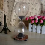Elegant sand timer with black sand flowing through glass, set on a copper-colored base, ideal for educational and decorative purposes.
