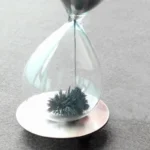 Close-up of a magnetic ferrofluid in an hourglass-shaped glass container, demonstrating magnetic field effects with black ferrofluid particles forming a spiky pattern.