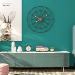 Modern geometric wall clock with gold hands on teal wall.