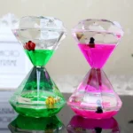 Decorative glass hourglass filled with vibrant green and pink water, featuring small fish figurines inside, perfect for educational or decorative purposes.