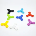 Colorful fidget spinners in black, blue, red, green, yellow, white, and purple arranged on a white background, showcasing their three-pronged design for stress relief and focus.