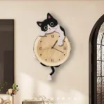 A playful wall clock featuring a black and white cartoon cat with big eyes, perched on a round wooden clock face. The clock combines functional timekeeping with charming decor, perfect for animal love.